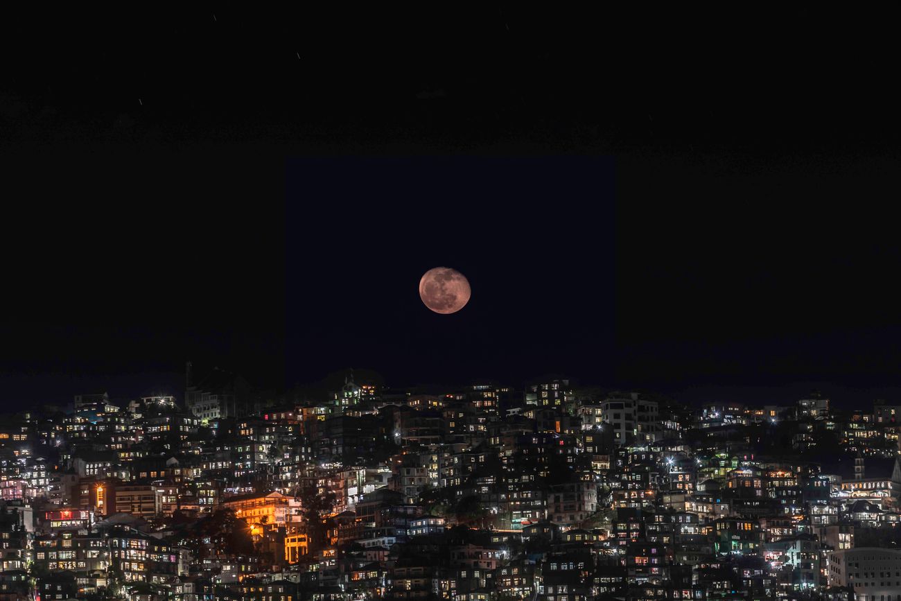A view of the moon shining over the city of Lunglei, Mizoram in the dark night as the buildings turn into silhouettes and their lights add to stars in the never-ending sky