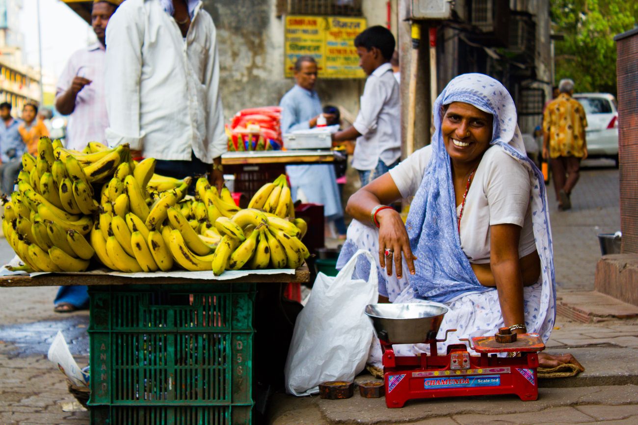 A woman in Mumbai smiles for the camera as she sells bananas on a crowded street of the city