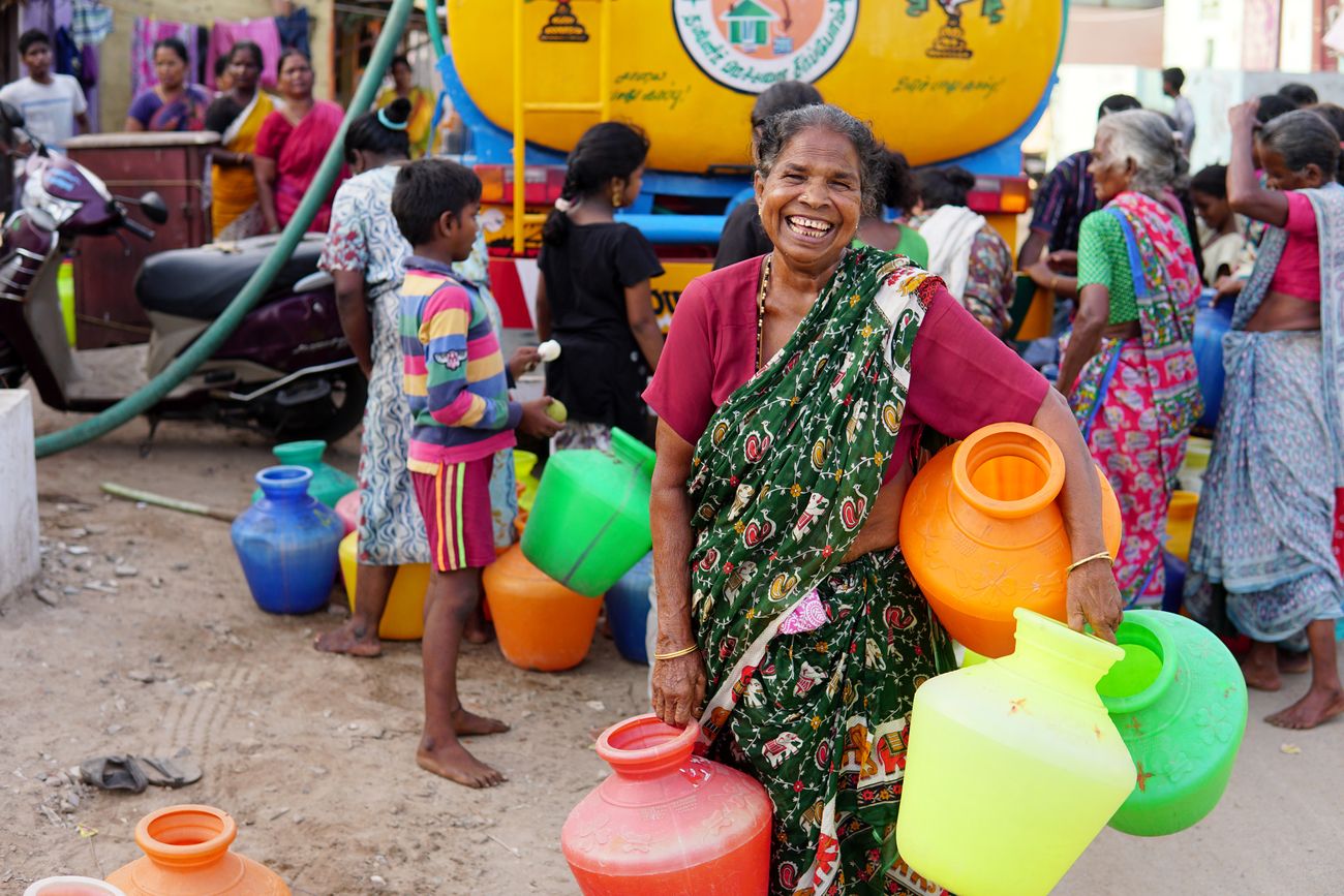 A woman smiles for the camera before collecting water in her colorful containers during the drought season