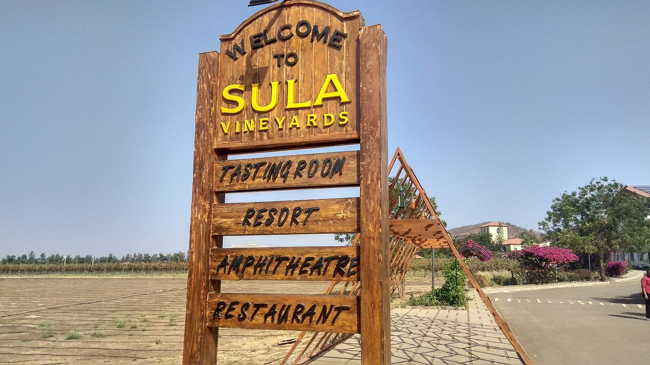 A wooden sign board with information welcomes the visitor to Sula Vineyards