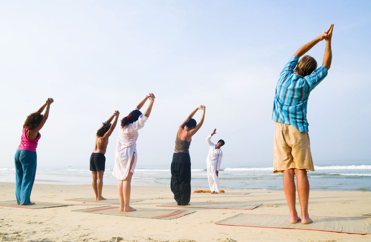 A yoga instructor instructs eager students by the beach early in the morning as the waves crash on the sand alongside the sea breeze.