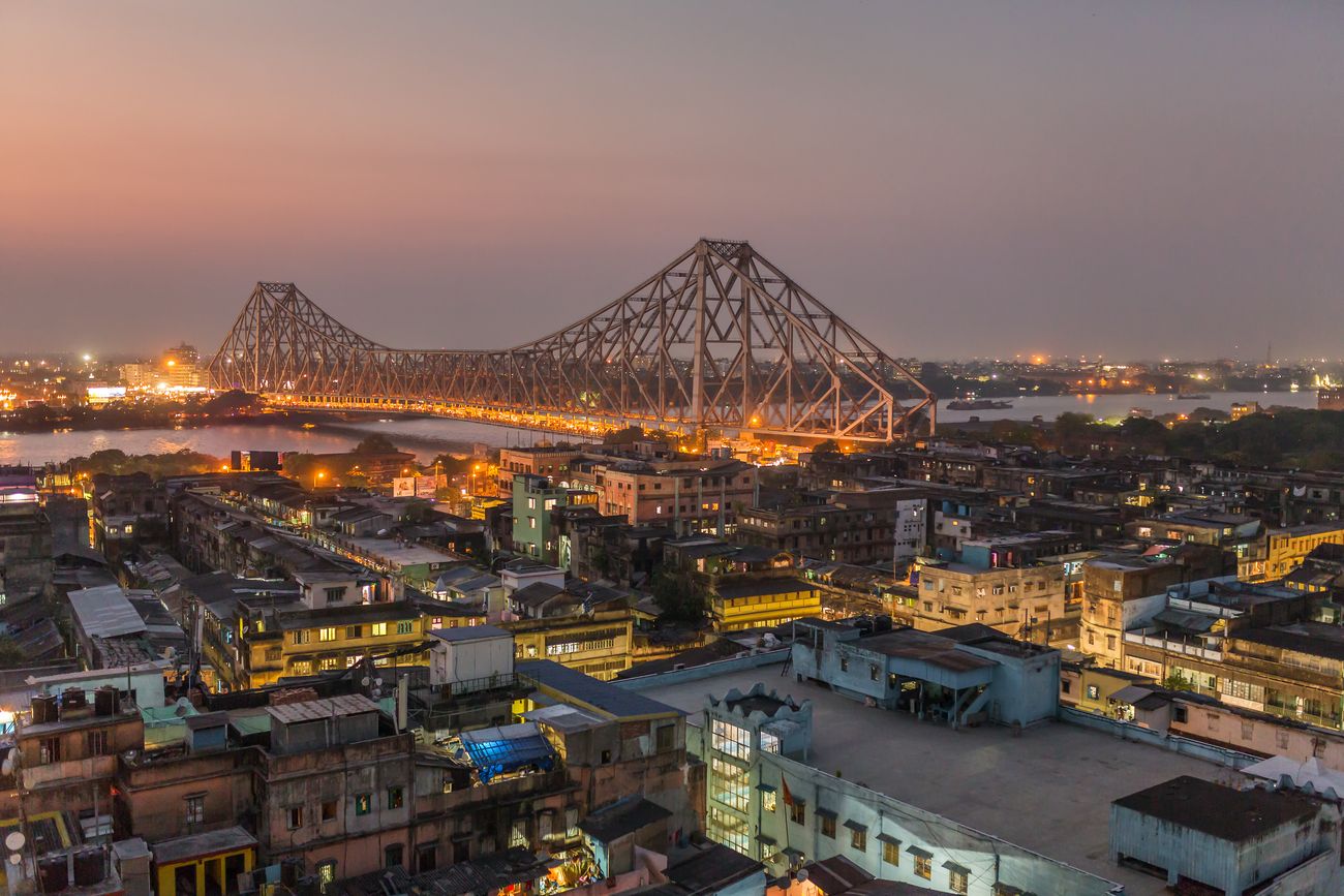 An aerial shot of the Howrah Bridge across River Hooghly at the time of twilight, and the parts of Kolkata that surround it 