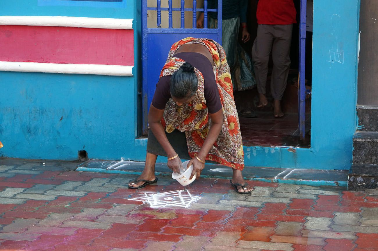 An Indian woman painting a kolam, using rice flour, on her doorstep. These signs are believed to bring prosperity to the residents of the house