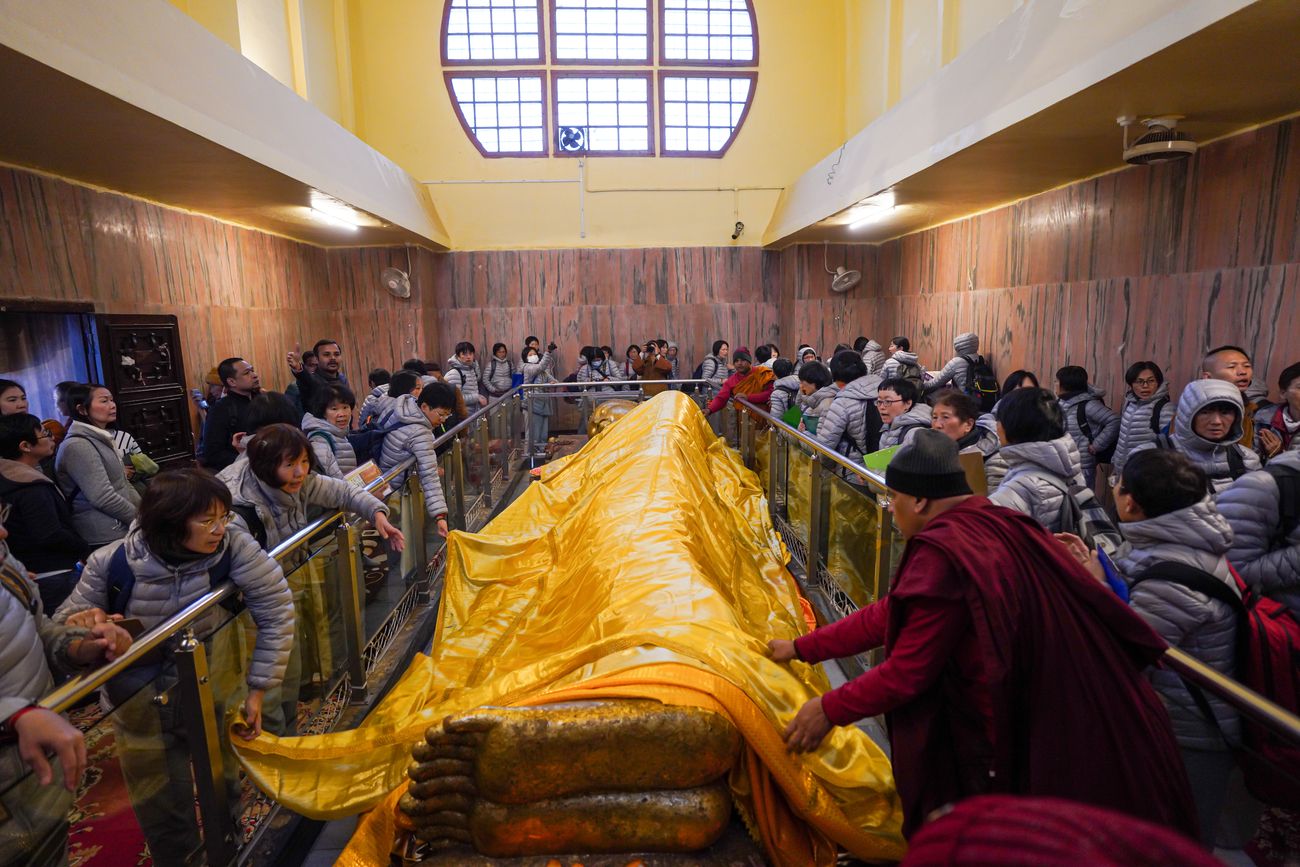 Devotees worship the reclining Buddha statue with a large golden fabric in Kushinagar, India