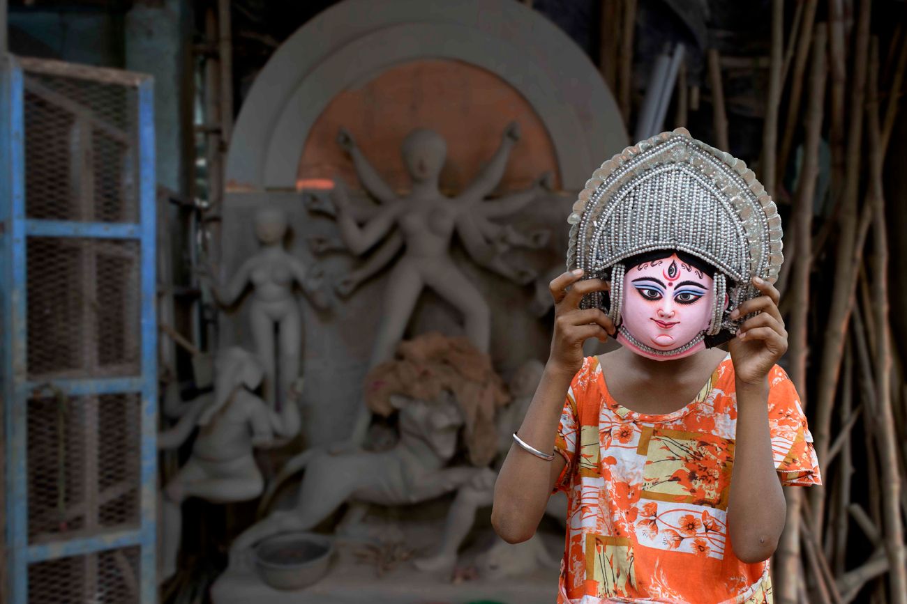 girl child stands posing with a paper mask of Goddess Durga from Purulia at the potters district in Kumortuli, North Kolkata. Kumaratuli, in north Kolkata, along the Hooghly river, is home to the city's famed clay idol-makers. While traditionally these artisans made idols only during the various pujas. most notably the Durga Puja, these days, many of them also work on sculptures for movie sets 