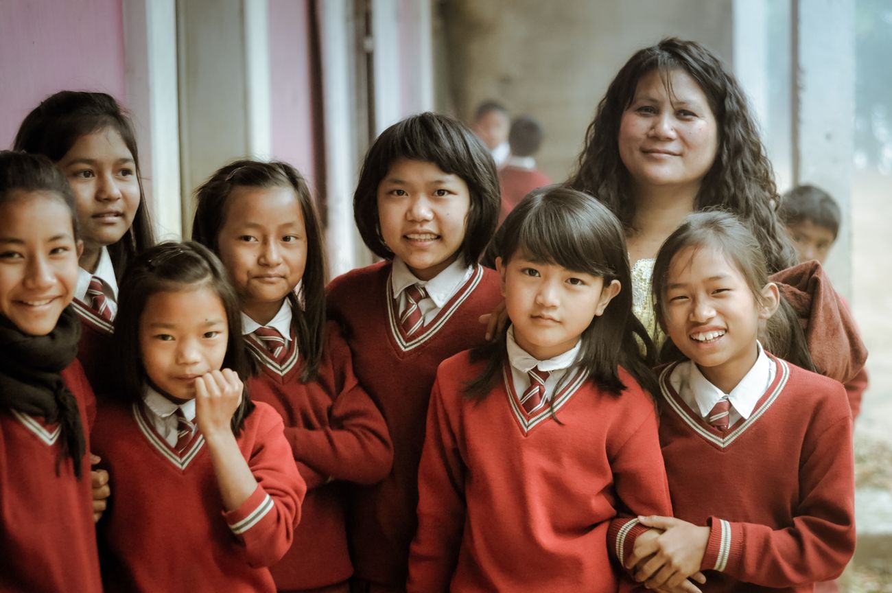 Girls dressed in red school uniforms and their teacher sport a smile for the camera at their school in Lungdai, Mizoram 