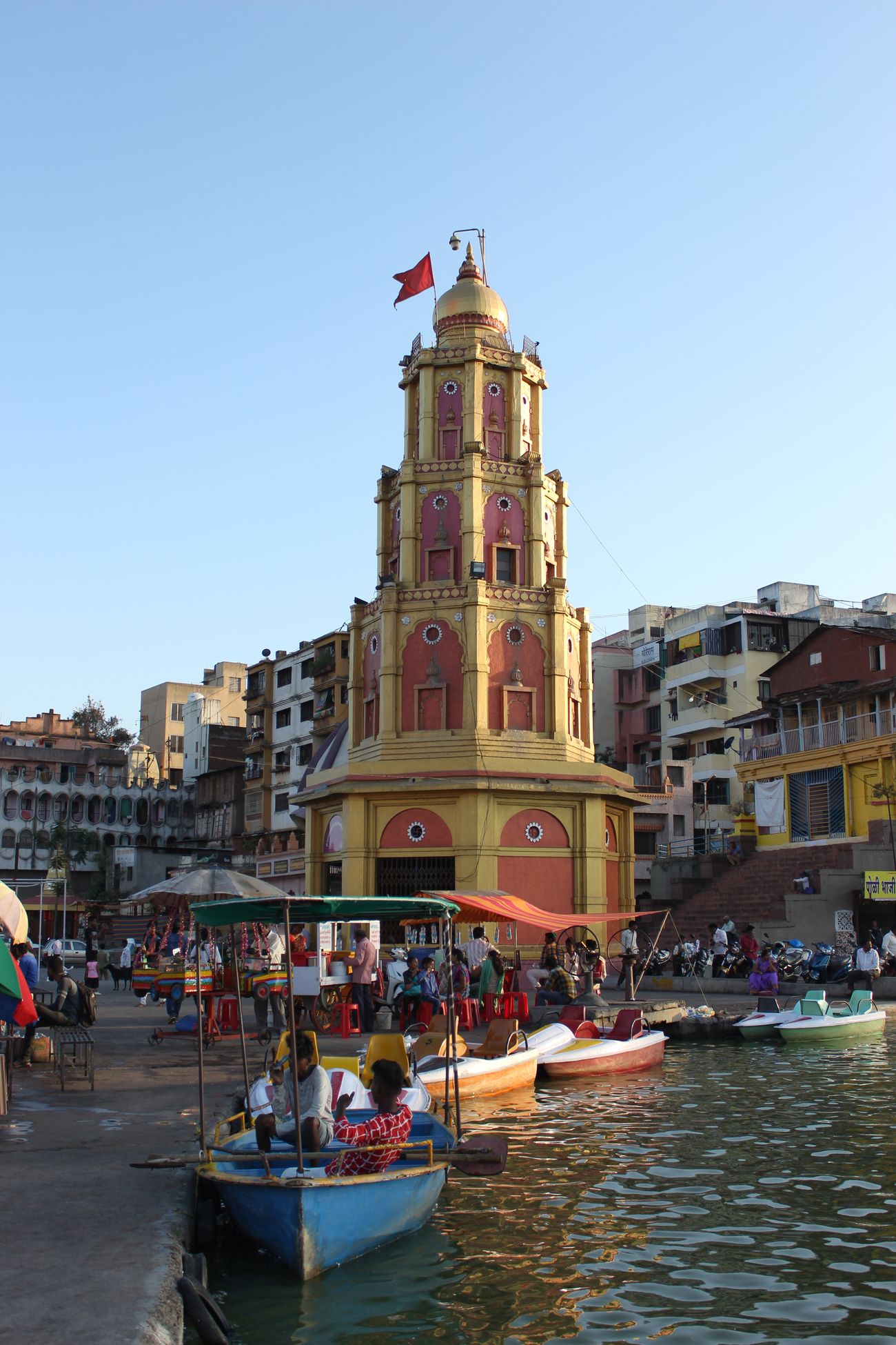 People taking a boat trip at the beautiful red and yellow Yashwantrao Maharaj Sadhu Dev Mamledar Temple