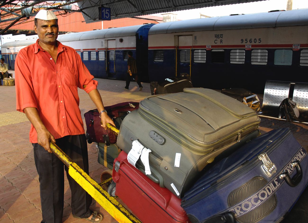 Porter (known as coolie in India) in red universal uniform carrying luggage of passengers at Mumbai Railway Station