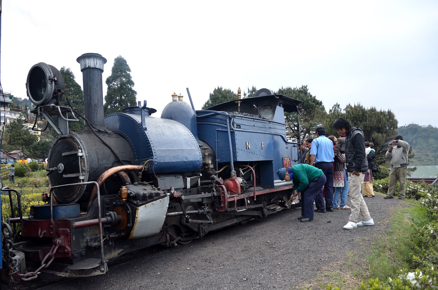 The Toy Train stops at Batasia War Memorial station in Darjeeling and people walk and go around the engine while looking over the lovely valley below 