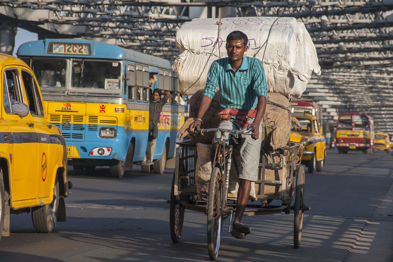 Traffic on the landmark Howrah Bridge with a rickshaw-puller, taxis, and public transportation bus