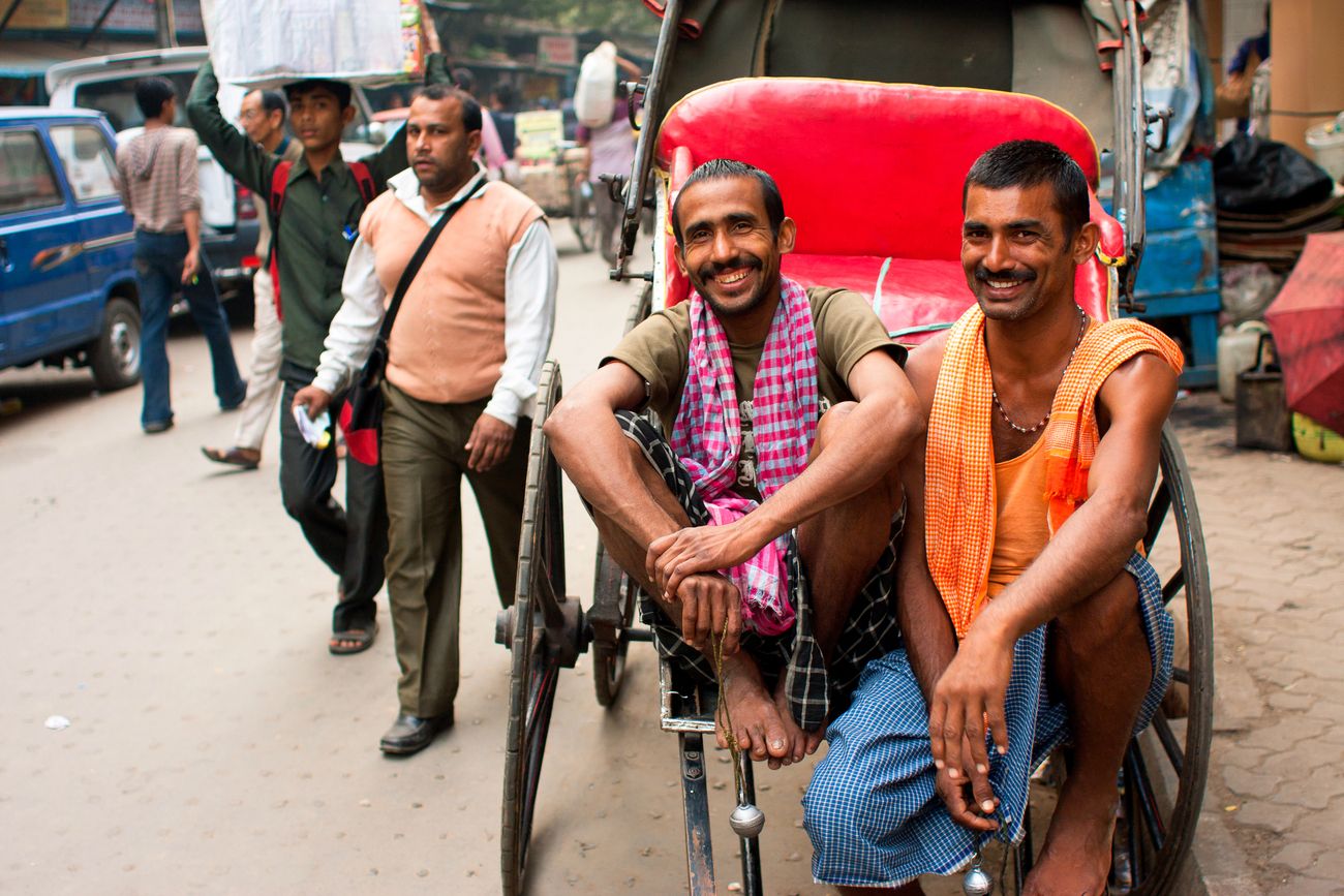 two hand-held rickshaw pullers sitting and smiling as they pose during some free time