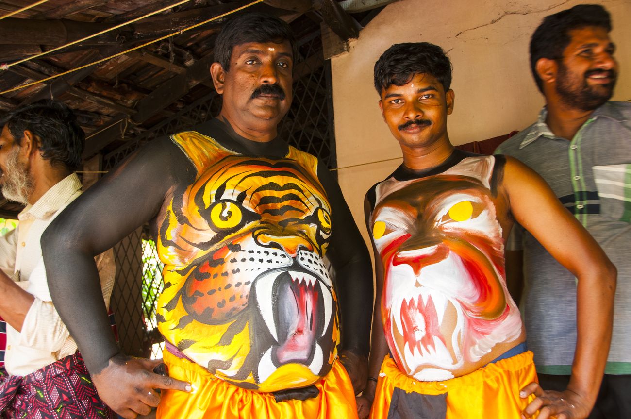 Two men posing for the camera with tigers painted on their torso by hand, in preparation for the Tiger Dance as a part of Onam celebrations.