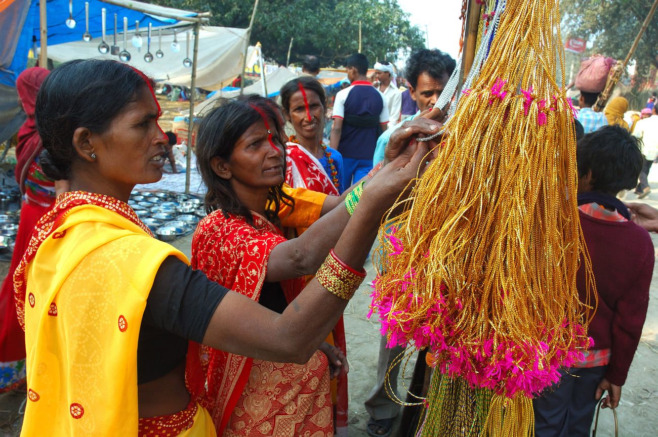 Women, streaked with bright red sindoor from nose tip to hairline, looking at decoration objects in the bazaar of Sonepur